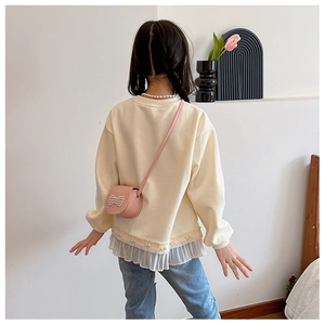 Détail d'un mini sac rose avec nœud perlé sur un sweat-shirt beige pour filles