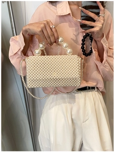 Detail of elegant pearl woven handbag with top handle and crossbody chain strap on a model
