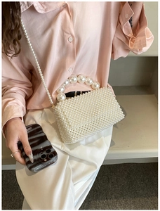 Detailed view of women's woven pearl handbag showing dense pearl texture and long strap