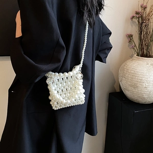 Sac à bandoulière tressé en perles blanc cassé porté par un mannequin sur une veste