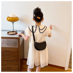 Detail of minimalist black semi-circle crossbody bag styled with a white girl's dress