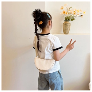 Minimalist beige semi-circular crossbody bag for kids shown on a child model with casual outfit