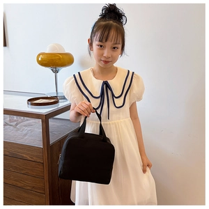 Minimalist black canvas tote bag carried by a child in a cozy home setting