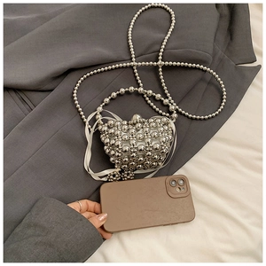 Close-up of heart-shaped silver beaded mini bag with white ribbon bow and chain strap