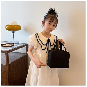 Close-up of black canvas lunch bag with zipper and woven handles held by a child
