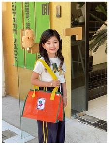 Fille tenant un sac de plage en maille orange avec liseré vert et broderie florale