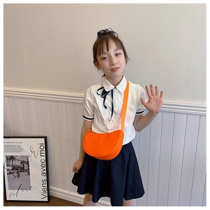 Detail of bright orange semi-circle crossbody bag styled with a white ruffled shirt
