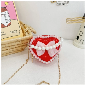 Detail of red heart-shaped kids bag with pearl handle, pink bow and gold chain strap
