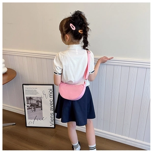 Detail of pink semi-circular crossbody bag with adjustable strap worn by a child