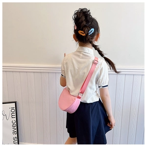 Pink semi-circle crossbody bag shown on child model wearing school uniform with braids