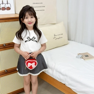 Girl's white t-shirt with bow and grey pleated skirt paired with a red heart pearl bag