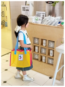 Détail du sac de plage enfant en maille jaune avec poignées bleues et patch fleur soleil