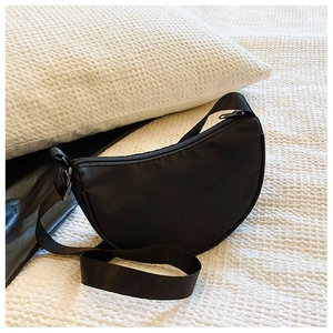 Detail of a black semi-circular nylon crossbody bag with adjustable strap on white bedding