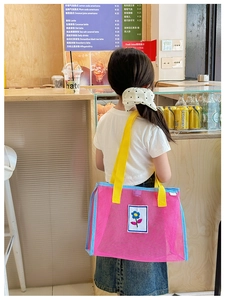 Détail du sac bandoulière en maille rose avec écusson fleuri et lanières jaunes