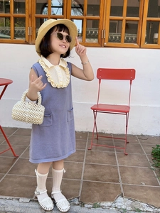 Girl wearing purple knit dress with woven pearl handbag and straw hat in sunny garden