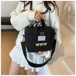 Detail of cute bear embroidery and woven label on a black canvas diaper crossbody bag
