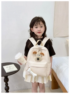 Detail of cream children backpack with 3D plush puppy and bone zipper charm on a girl