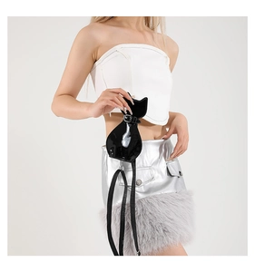 Detail of black patent leather cat-shaped mini crossbody bag with glossy finish on model