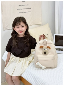 Detail of cute cream kid backpack with plush dog head and bone zipper pull accessory