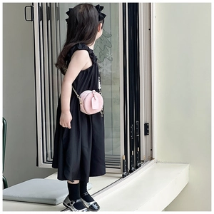 Fille portant un sac à bandoulière rond rose avec chaîne dorée et robe noire sans manches