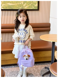 Detail of cute purple kids backpack featuring a plush puppy head and bone charm