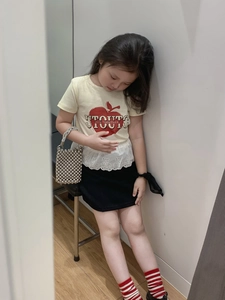 Close-up of girl's yellow T-shirt with apple print, lace hem and silver pearl woven bag