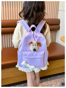 Detail of a purple kids backpack featuring a plush dog head and bone pendant detail