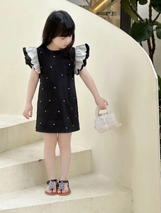 Detail of child wearing a black dress with pearl accents and ruffled flutter sleeves