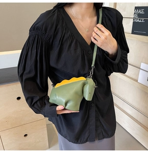 Détail d'un sac bandoulière dinosaure vert en cuir avec écailles jaunes et boucle en métal