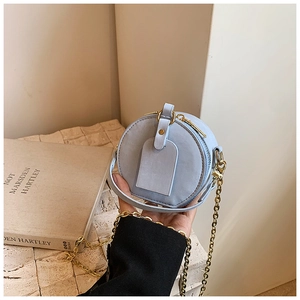 Détail du mini sac rond bleu clair avec chaîne dorée et étiquette décorative