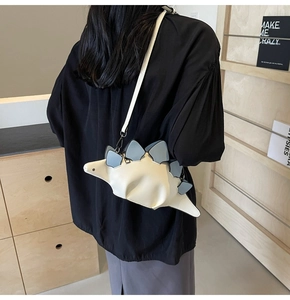 Detail shot of a cream dinosaur crossbody bag worn by a model against a modern background