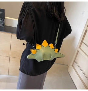 Detail of cute green dinosaur crossbody bag with orange spines worn by a model