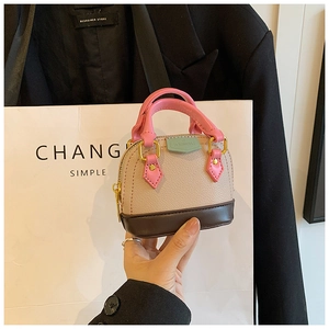 Mini sac coquillage en cuir litchi beige et rose tenu sur un fond de costume noir chic