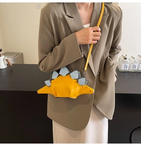 Detail of creative yellow dinosaur crossbody bag with blue back fins shown on a model