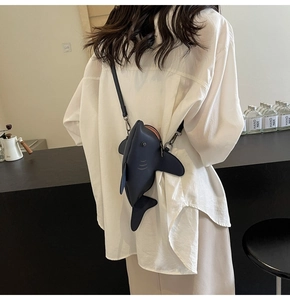 Détail d'un sac bandoulière en forme de requin bleu foncé porté par un mannequin dans un café