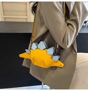 Detail view of a yellow stegosaurus-shaped crossbody bag with blue fins and metal buckles