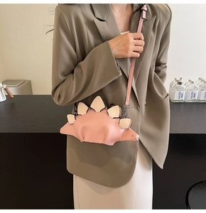 Detail of pink cartoon dinosaur shoulder bag with adjustable strap on a green blazer outfit