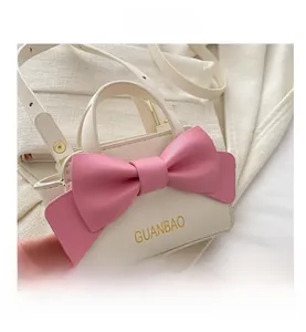Detail shot of mini white tote bag featuring a large pink bow and gold strap buckle