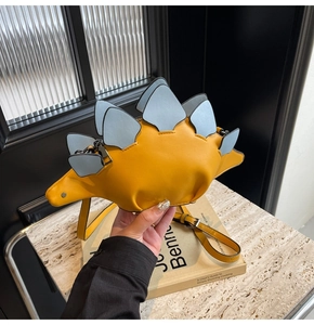 Detail shot of a yellow stegosaurus-shaped shoulder bag featuring blue scales and metal hardware