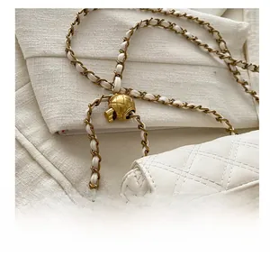Close-up of white quilted leather texture with gold metal chain and adjustable ball buckle