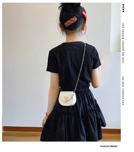 Close-up of a child wearing a white leather heart-shaped bag with a golden metal chain