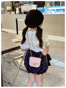 Pink quilted mini crossbody bag with gold chain strap worn by a child in a cafe