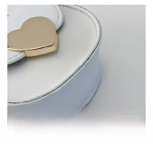 Detail showing precise stitching and golden heart metal decoration on white leather bag