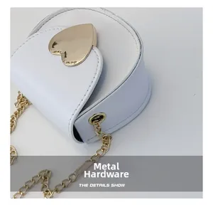 Detail of white heart-shaped crossbody bag featuring golden hardware and metal chain strap