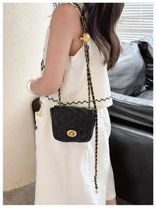 Close-up of black quilted mini bag with adjustable gold ball chain and metal lock