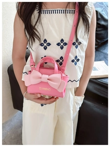 Pink kids crossbody bag with large bow detail shown on a girl in a home setting