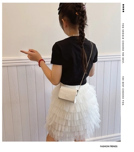 Detail of a white faux crocodile skin mini chain crossbody bag worn by a girl