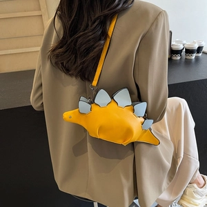 Cute yellow dinosaur shaped crossbody bag with blue scales worn by a model in a cafe