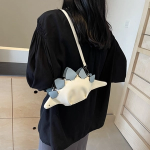 Cartoon stegosaurus shoulder bag in cream and grey blue, shown on model in interior setting