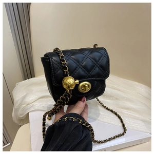 Detail of black quilted mini crossbody bag featuring a gold chain strap and metal ball buckle